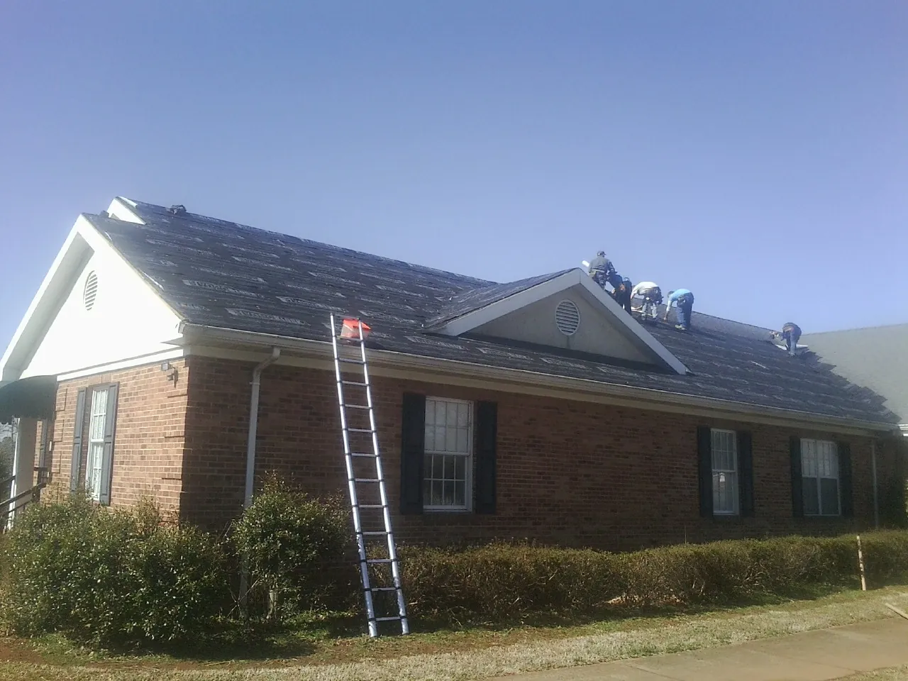 Crew tearing shingles off a brick ranch roof with a ladder set — Metal Roof Repair work by our crew in Joshua