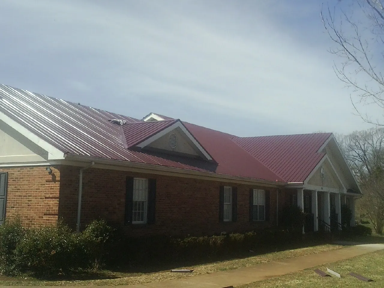 Red metal roof with gabled entries on a long brick building, from a Hail Damage Roof Repair job in Joshua