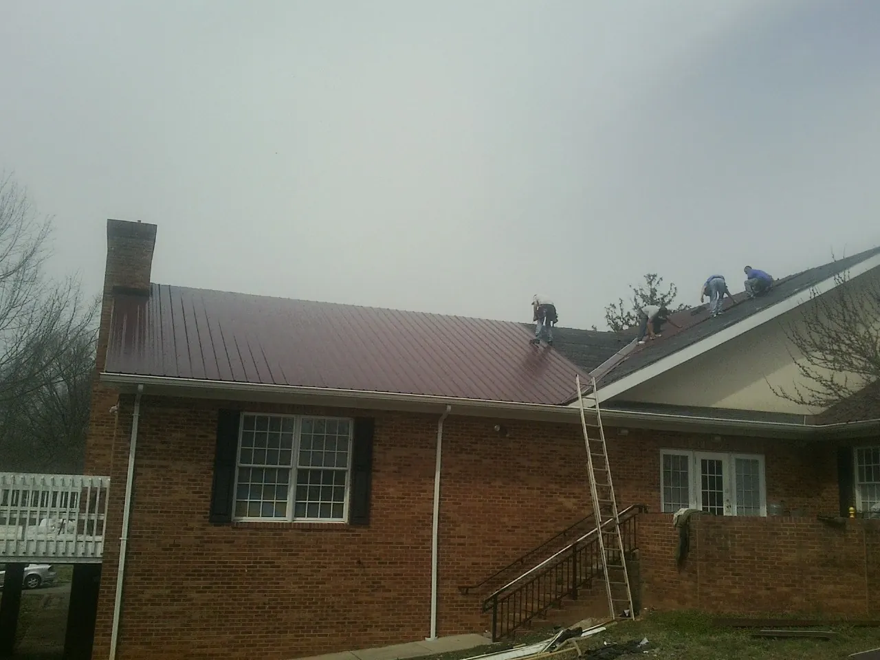Crew setting red metal roofing panels on a brick home in Joshua