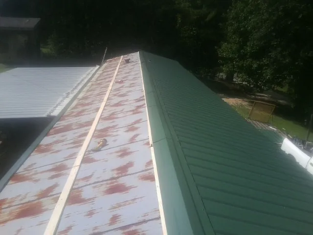 Old rusted panels beside newly installed green metal roofing — Wind Damage Roof Repair by Roofing Brothers in Joshua