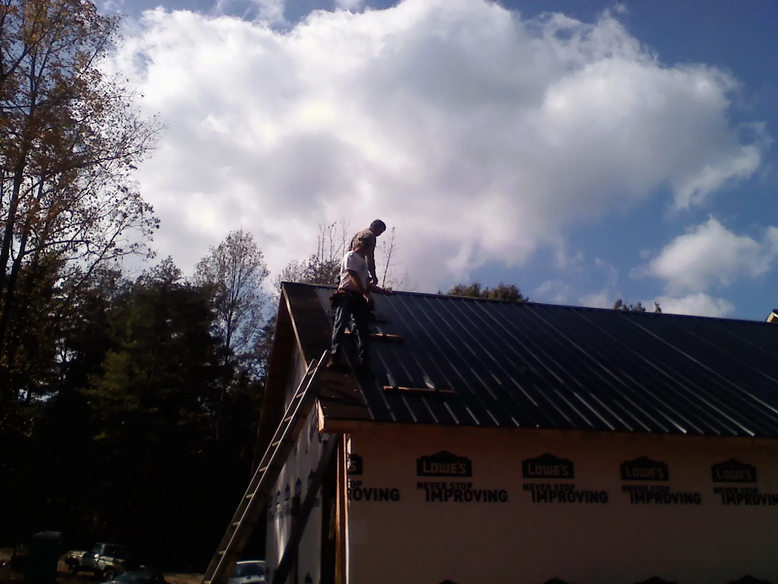 Roofer fastening dark metal panels high against a cloudy sky, from a Roof Inspection job in Joshua