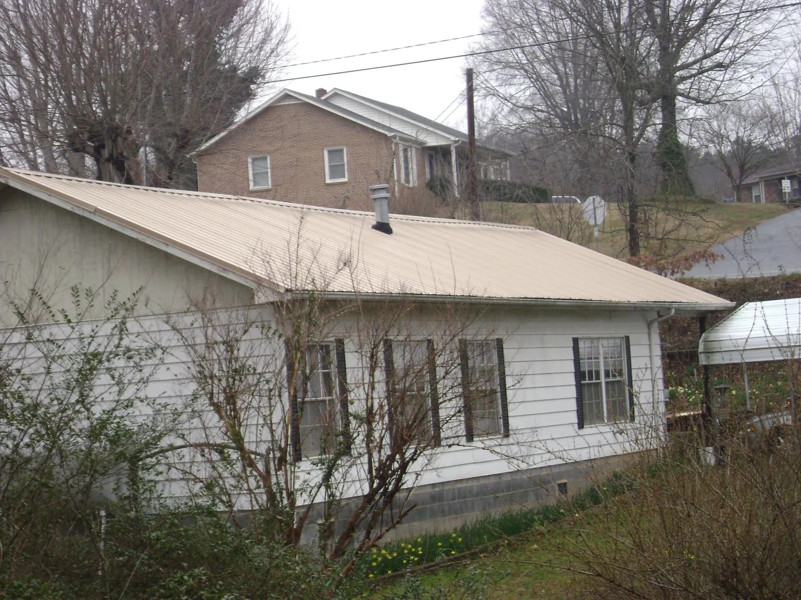 Tan metal roof on a white sided house set into a hillside — Commercial Roofing by Roofing Brothers in Joshua