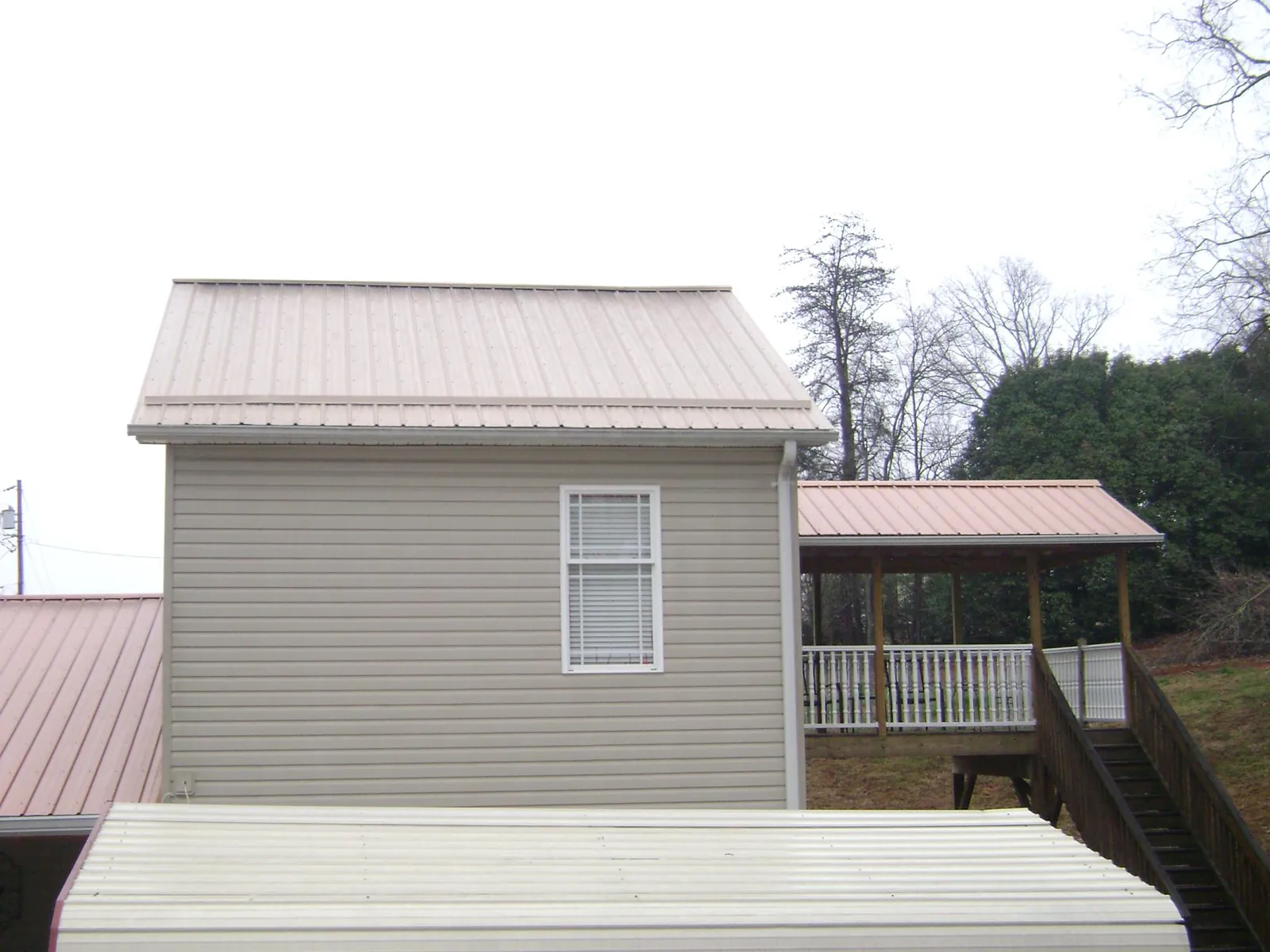 Tan metal roofs on a two story addition and attached porch, from a Roof Replacement job in Joshua